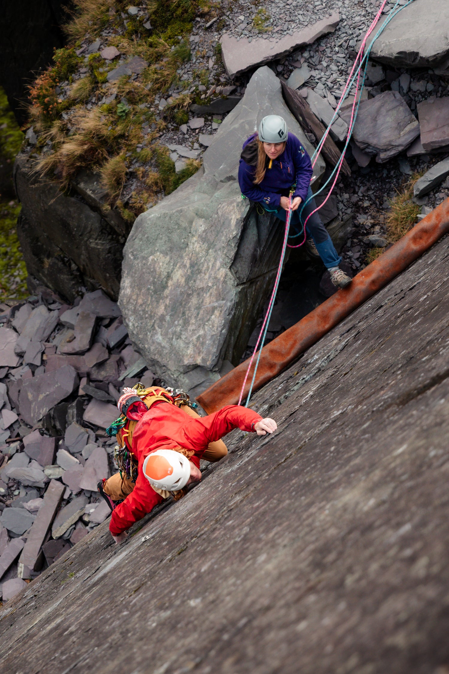 Two climbers on a rocky mountain face with ropes and climbing gear.