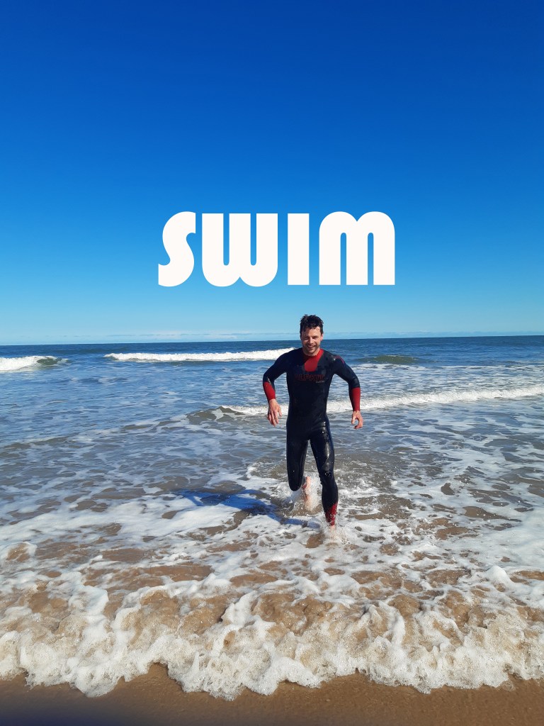 White lettering 'swim' James runs out of the ocean wearing a wetsuit.