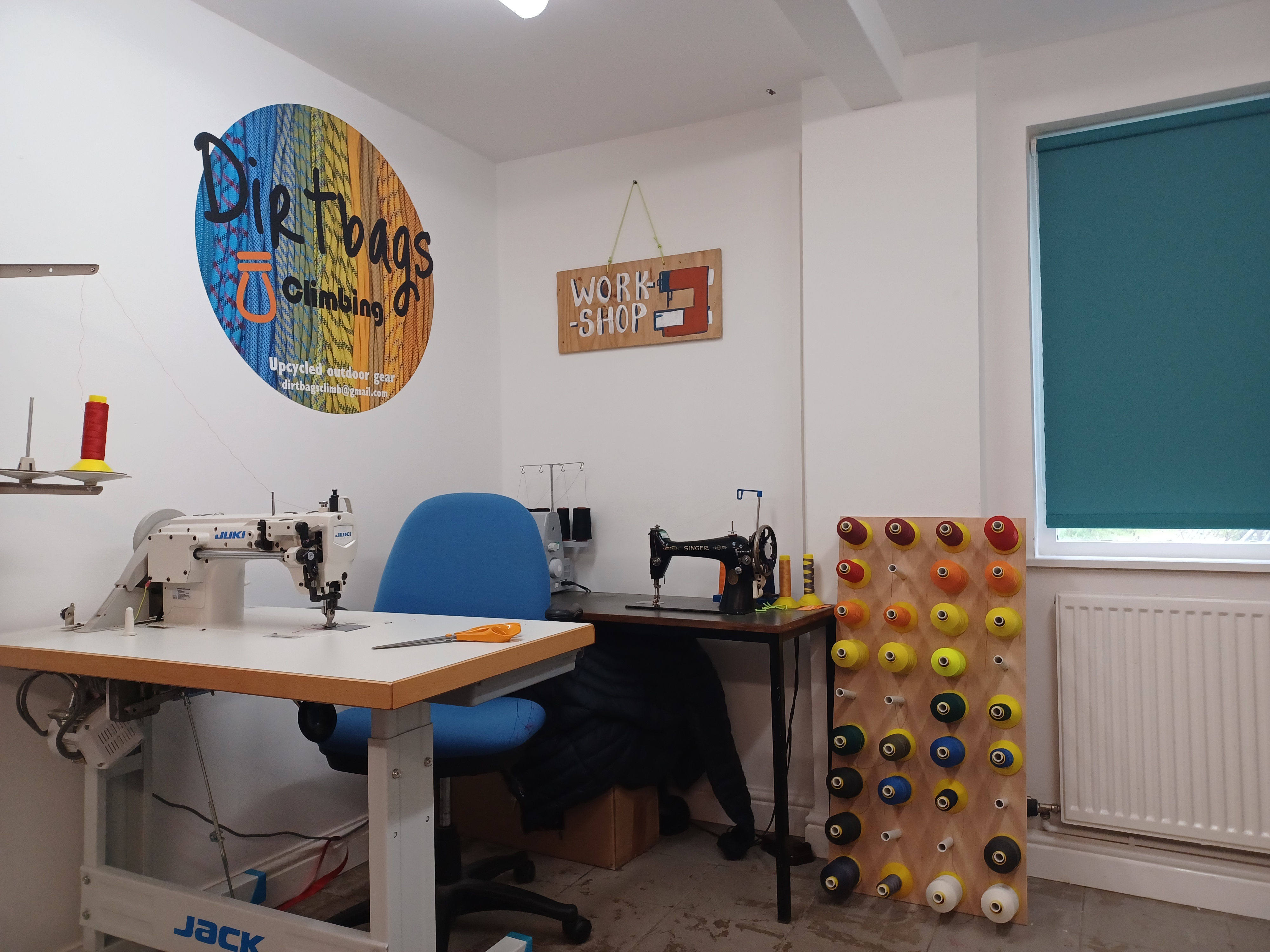 A corner of a workshop, with a sewing machine and an empty chair. A 'dirtbags climbing' sign is on the wall
